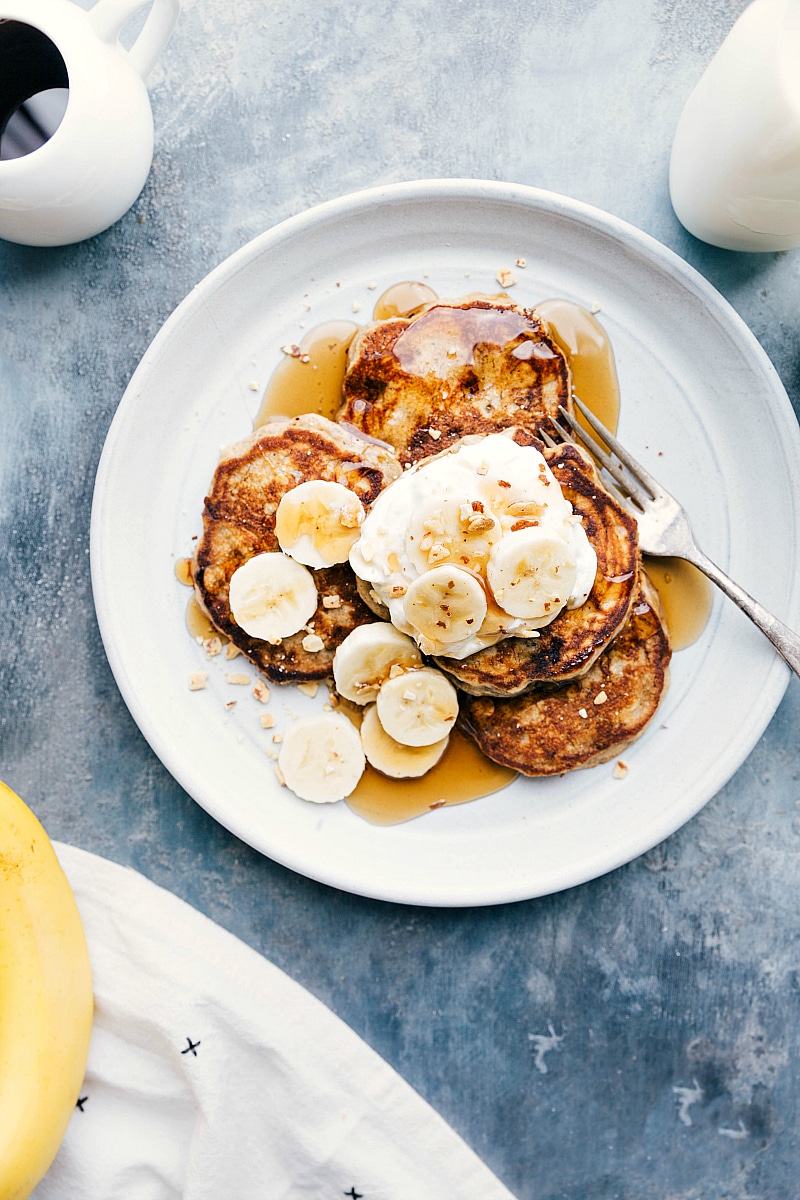Overhead image of the ready-to-eat Banana Pancakes with syrup and fresh bananas on top.