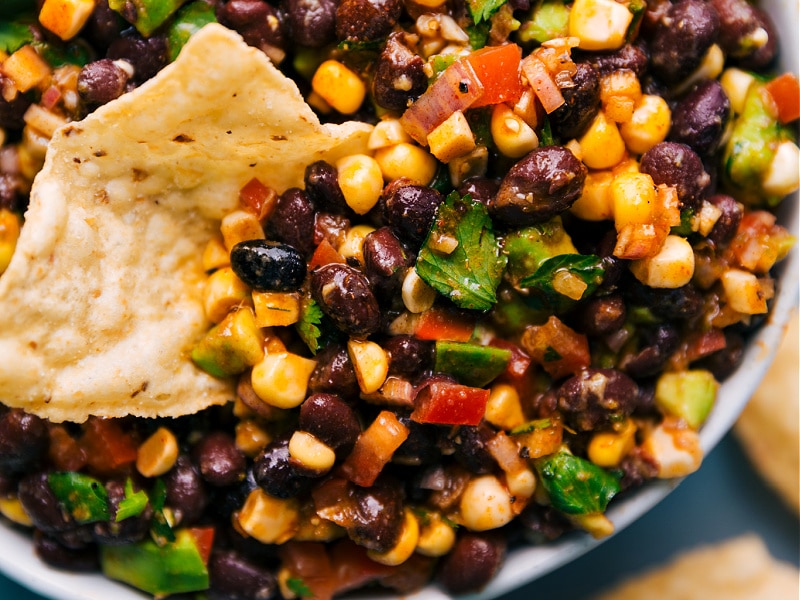 Image of the black bean corn avocado salad with a chip dipping into it