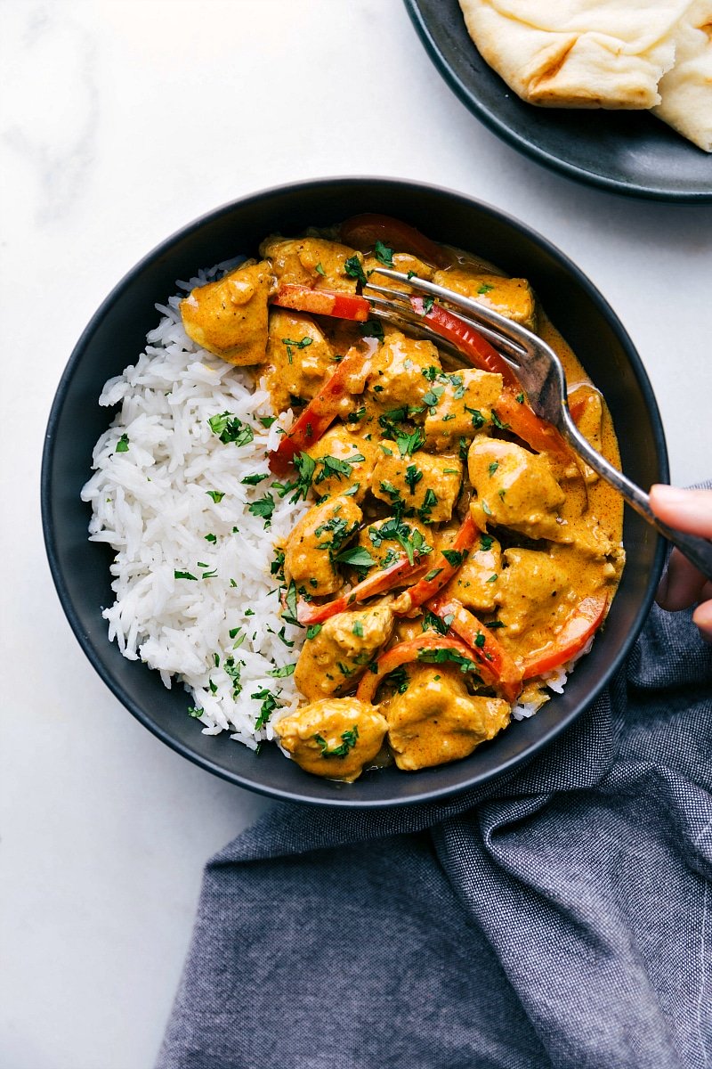 Image of the ready-to-eat Coconut Curry Chicken with a fork in it and rice on the side with naan bread.