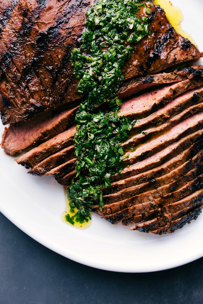 Overhead view of Grilled Flank Steak, sliced and topped with chimichurri sauce.