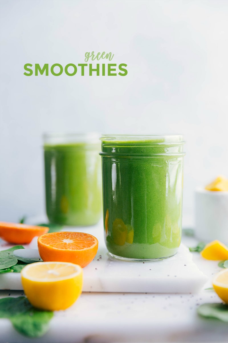 Two glasses on a table, full of Green Smoothie, and surrounded by citrus.