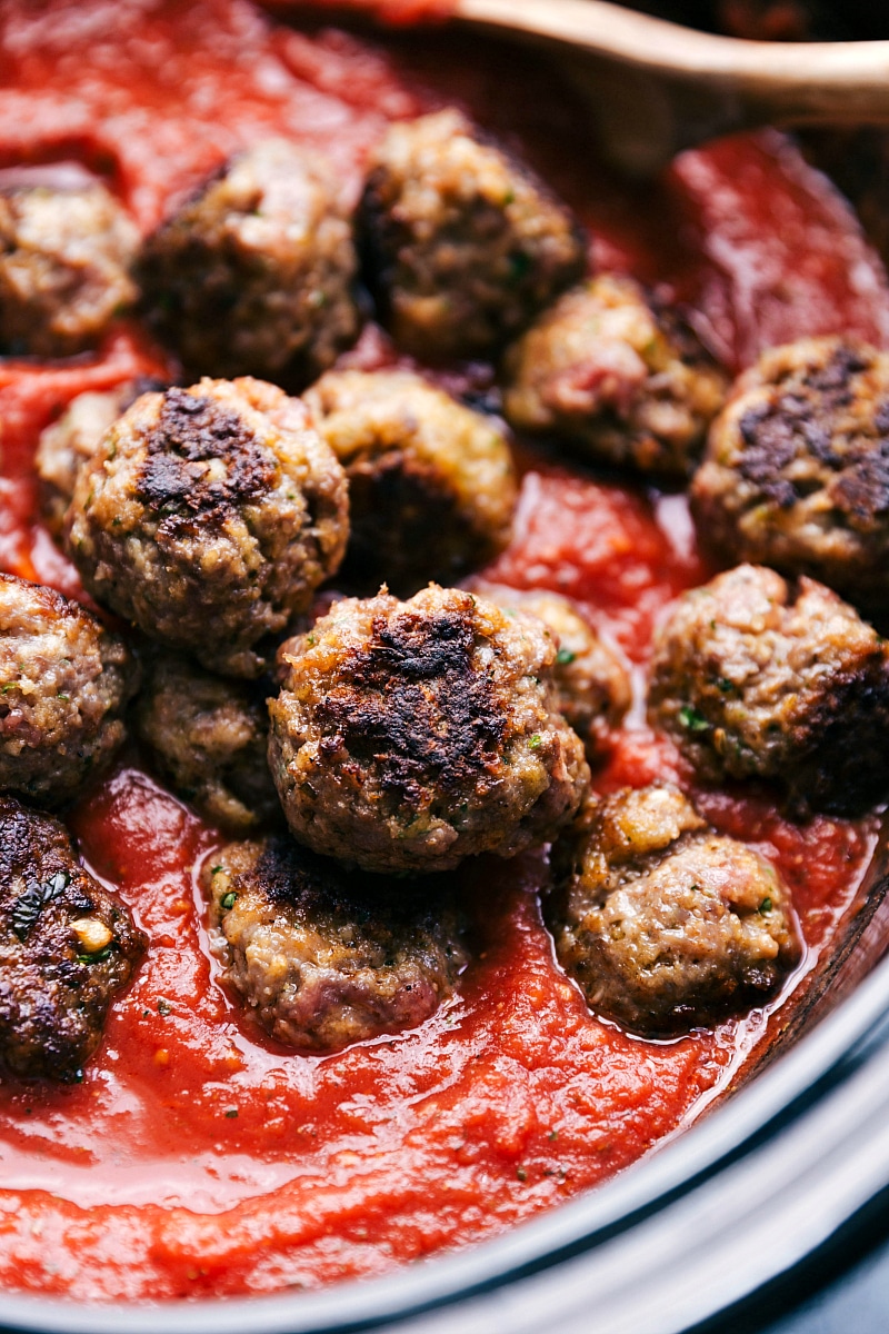 Up close image of the meatballs being put in marinara sauce for this meatball sliders recipe