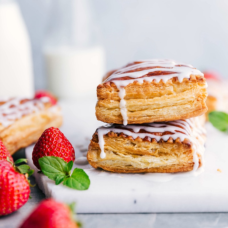 Image of two Toaster Strudels stacked on top of each other, with icing dripping and fresh strawberries on the side.